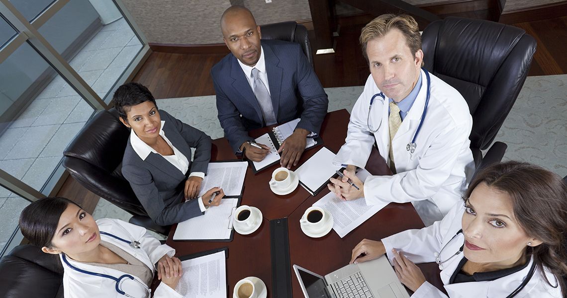 Doctors and Business people looking up toward camera, sitting around a meeting table